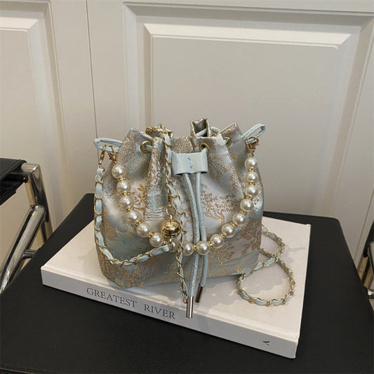 Decorative bucket bag with pearl embellishments on a book titled 'Greatest River'.