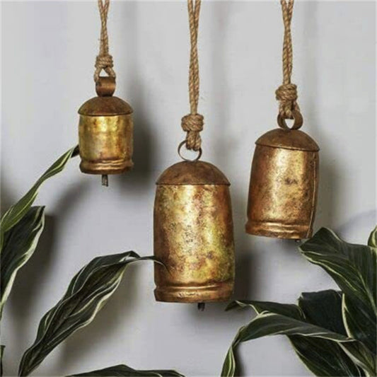 Three rustic gold bells hanging against a light background with green leaves.