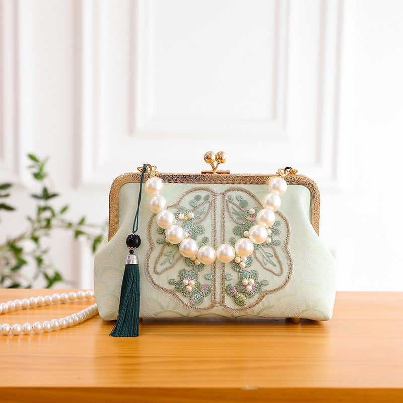 Decorative handbag with floral embroidery and a pearl necklace on a wooden surface.