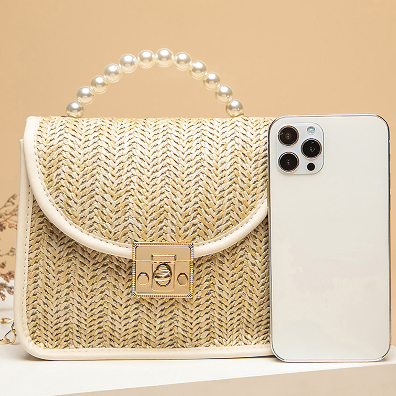 Beige woven handbag with pearl handle next to a smartphone on a beige background