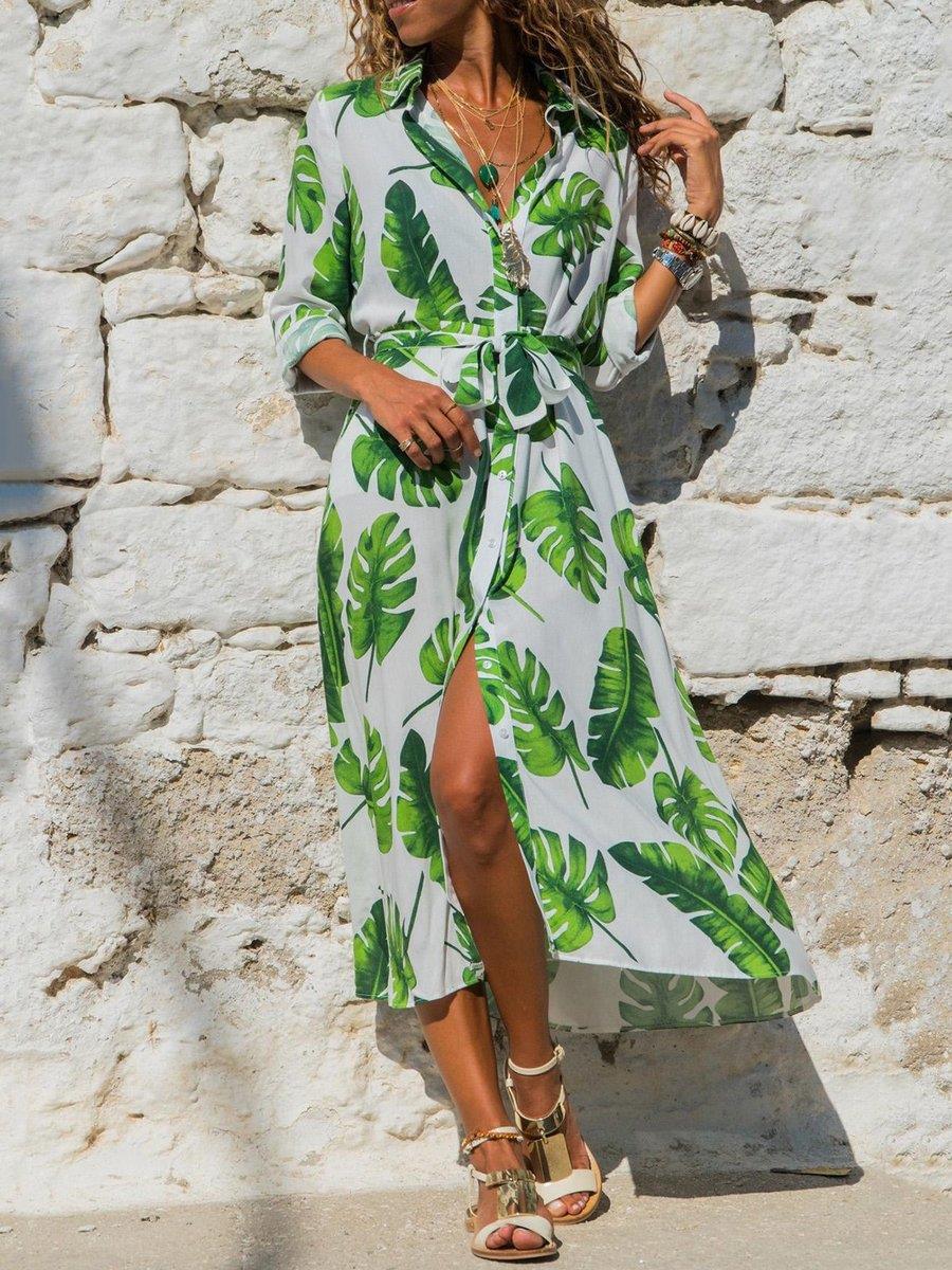 Woman wearing a tropical leaf print dress against a stone wall.