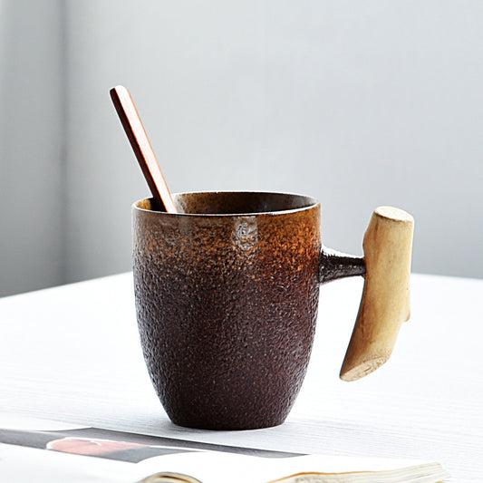 Brown ceramic mug with wooden handle and spoon on a white surface