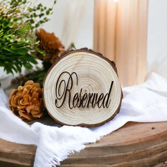 Wooden round sign with 'Reserved' text on a table with flowers and white cloth.