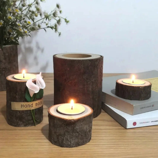 Wooden candle holders with candles on a wooden surface, with a vase of flowers in the background.