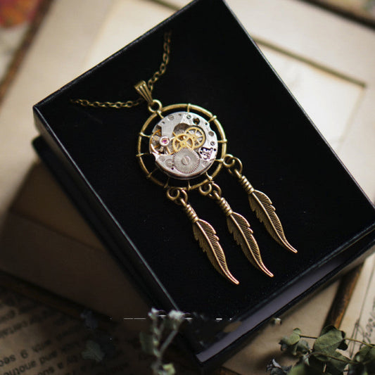 Steampunk-style necklace with mechanical components and feathers on a black box.