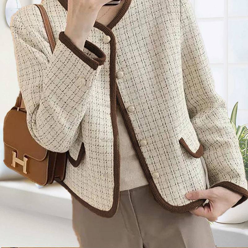 Person wearing a beige tweed jacket with brown trim holding a brown handbag.