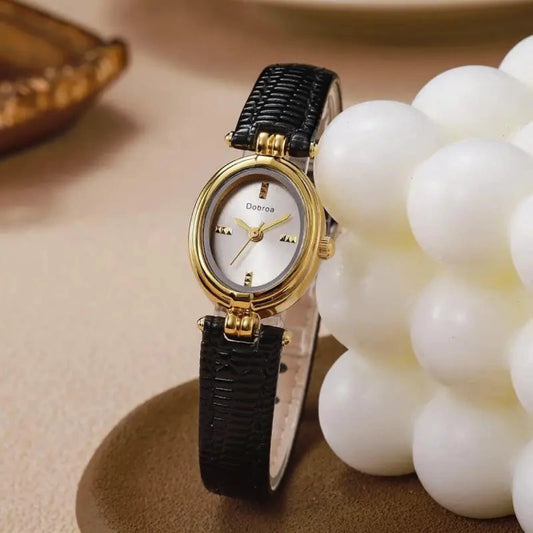 Gold watch with black strap on a beige surface with decorative elements