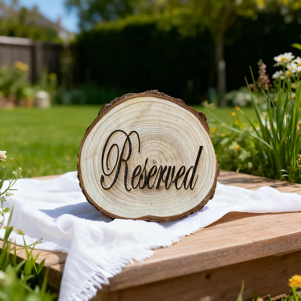 Wooden 'Reserved' sign on a picnic table outdoors with grass and flowers in the background