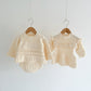 Two cream-colored baby outfits on hangers against a white background