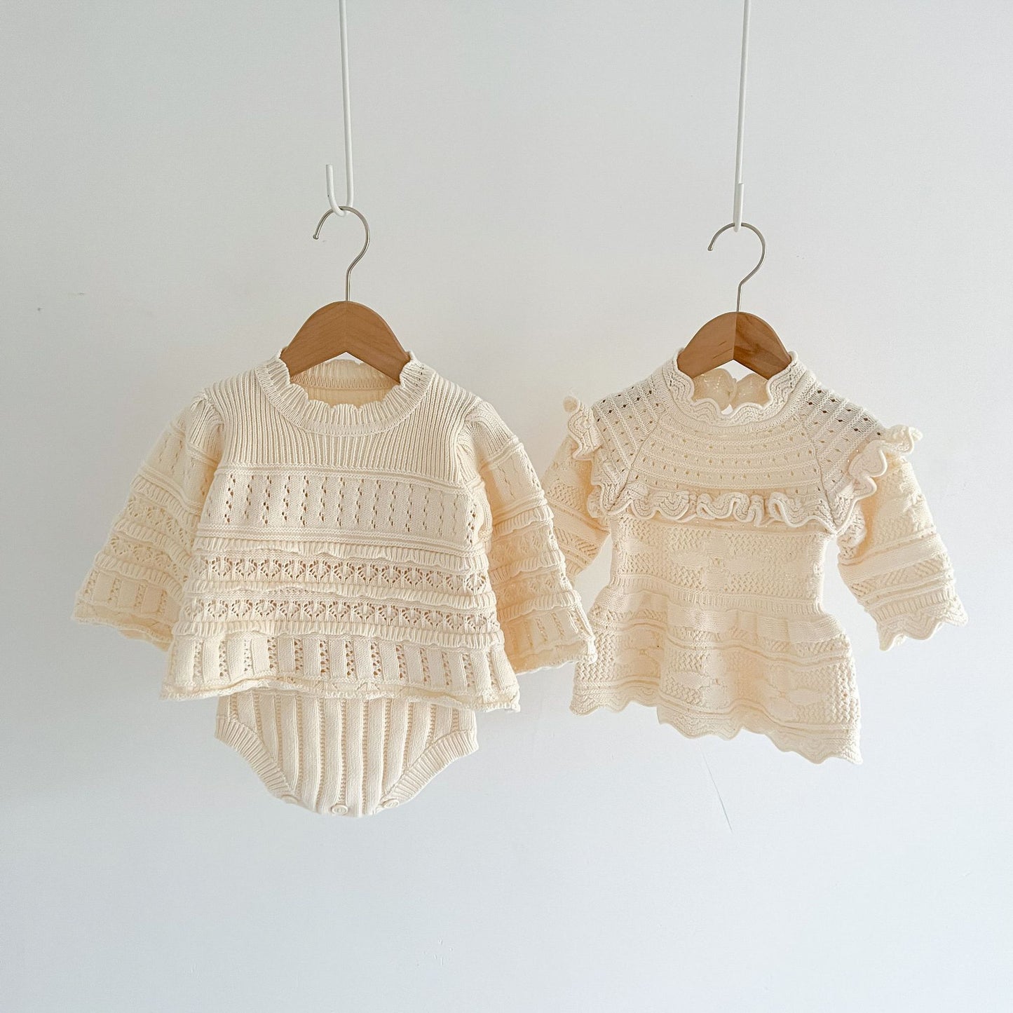 Two cream-colored baby outfits on hangers against a white background