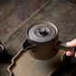 Person holding a black teapot on a wooden surface