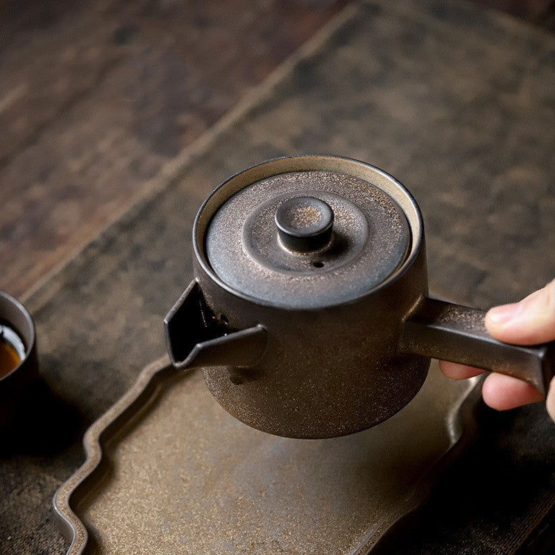 Person holding a black teapot on a wooden surface