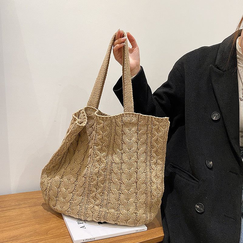 Person holding a beige knitted tote bag on a wooden surface with a white background