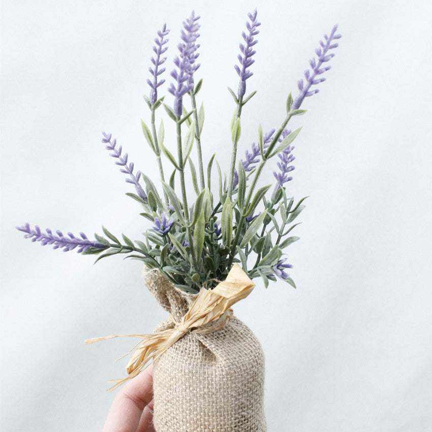 Artificial lavender plant in a burlap bag against a light background