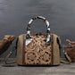 Brown leather handbag with intricate floral patterns on a dark surface