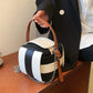 Black and white striped handbag with a brown handle and chain detail on a wooden surface.