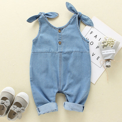 Blue denim baby romper with bow straps on a light beige background