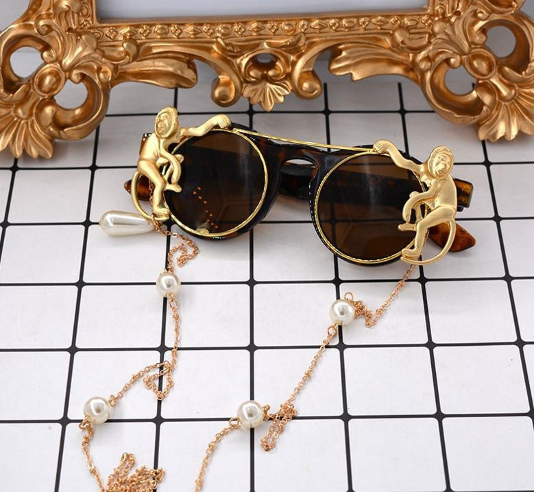 Sunglasses with decorative chain and gold monkey designs on a checkered background