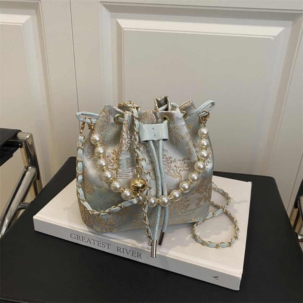 Decorative bucket bag with pearl embellishments on a book titled 'Greatest River'.