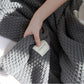 Gray textured blanket with a tag held by a hand on a white background