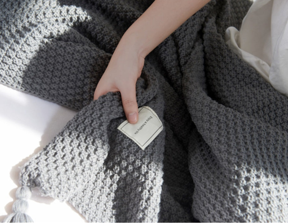 Gray textured blanket with a tag held by a hand on a white background