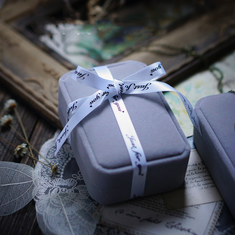 Gray jewelry box with a white ribbon on an old book