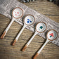 Four ceramic spoons with wooden handles on a wooden surface with newspaper underneath.