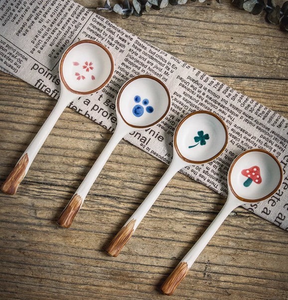 Four ceramic spoons with wooden handles on a wooden surface with newspaper underneath.