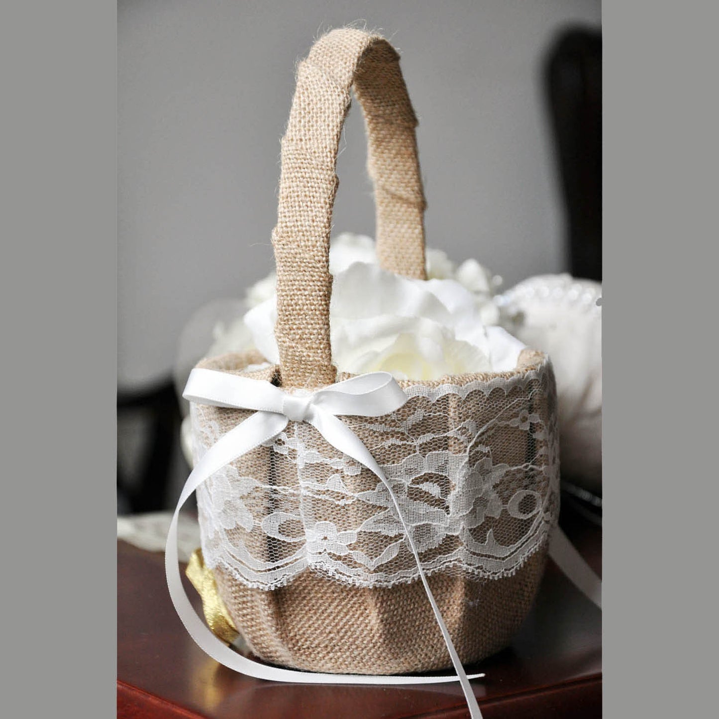 Burlap and lace flower girl basket with a white ribbon on a wooden surface.