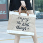 Person holding a beige tote bag with 'enjoy the little things' text.