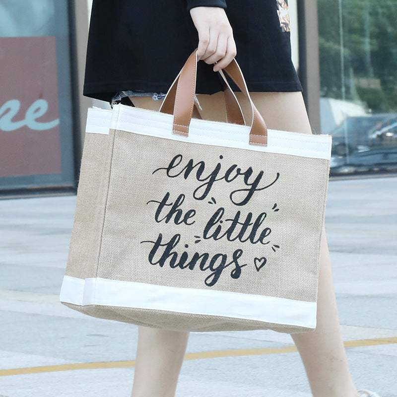 Person holding a beige tote bag with 'enjoy the little things' text.
