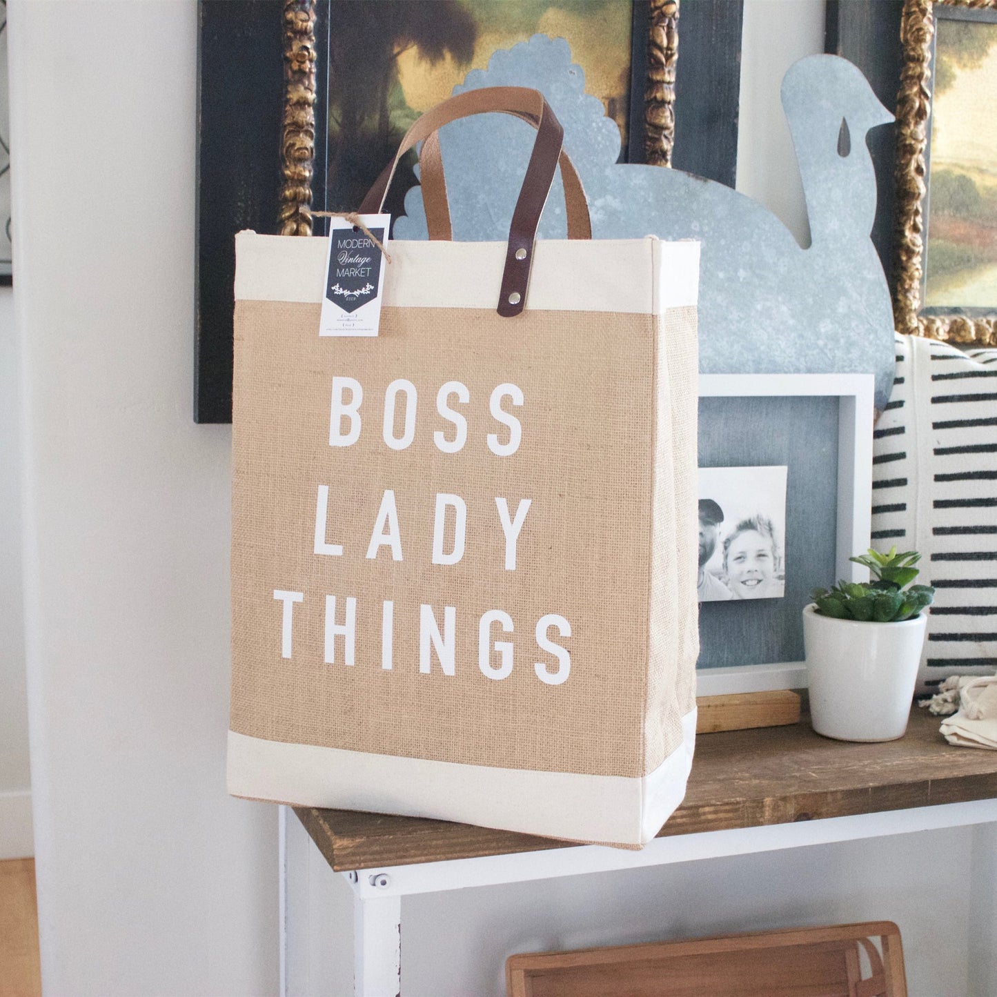 Tote bag with 'BOSS LADY THINGS' text on a shelf with decorative items.