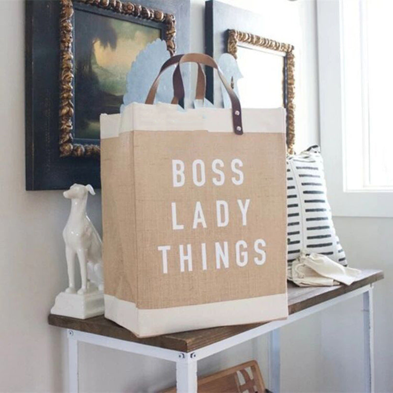 Beige tote bag with 'BOSS LADY THINGS' text on a wooden table.