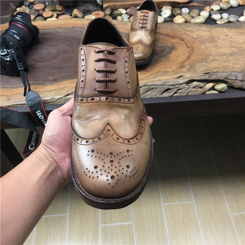 Brown leather shoe held by a hand with a camera and wooden surface in the background
