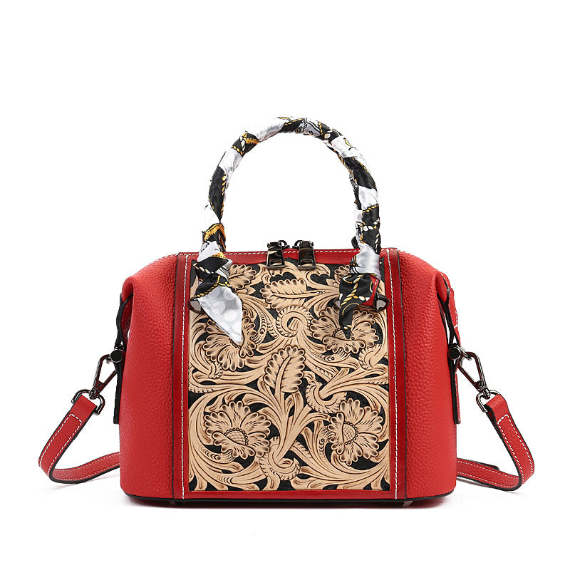 Red handbag with intricate floral tooled leather design on a white background