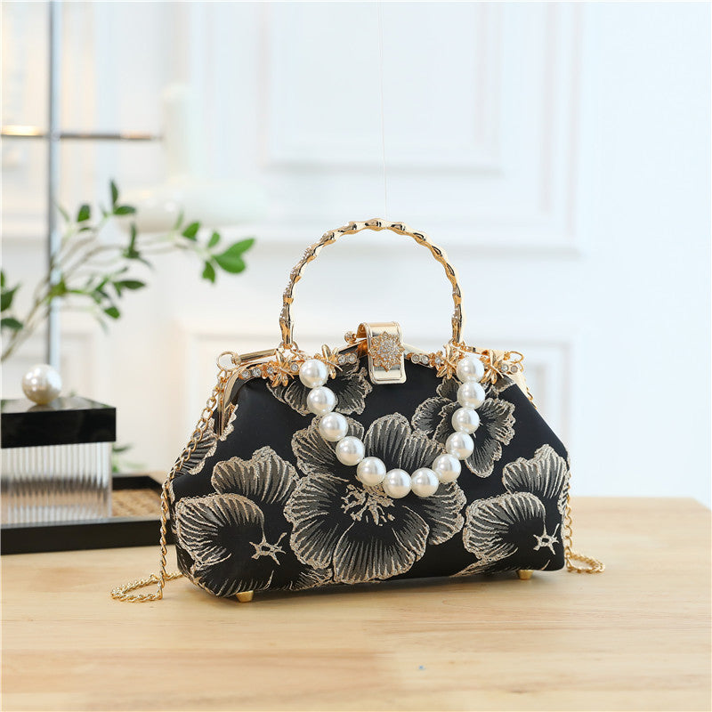 Black floral handbag with pearl embellishments on a wooden surface.