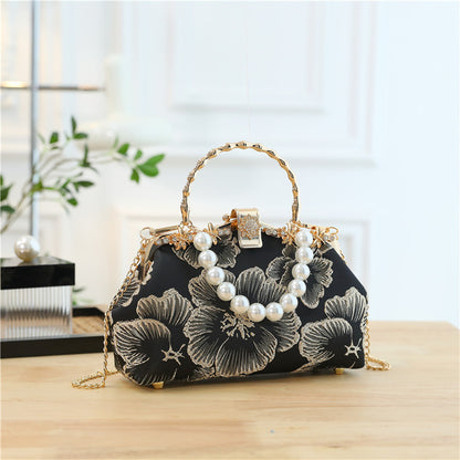 Black floral handbag with pearl embellishments on a wooden surface.