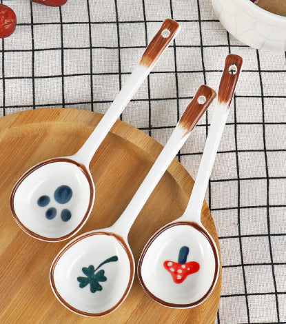 Set of three ceramic spoons with decorative handles on a wooden board.