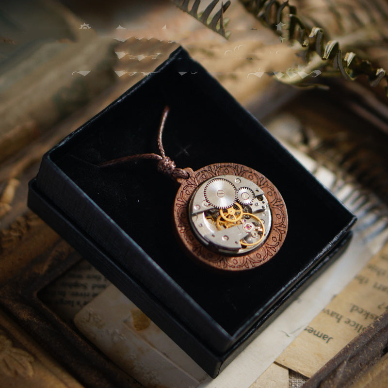 Steampunk-style necklace with mechanical heart pendant in a black box on vintage paper.