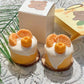 Two small orange and white cakes with decorative elements on a lace tablecloth.
