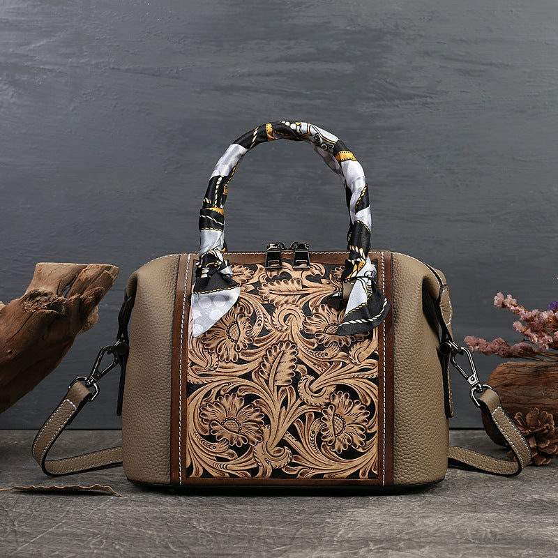 Brown leather handbag with intricate floral patterns on a dark surface