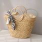 Woven straw bag with a decorative ribbon on a light surface.