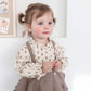 Child wearing a floral blouse and brown skirt against a white wall.