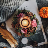 Decorative candle holder with flowers and pinecones on a magazine with a pumpkin and feather beside it.