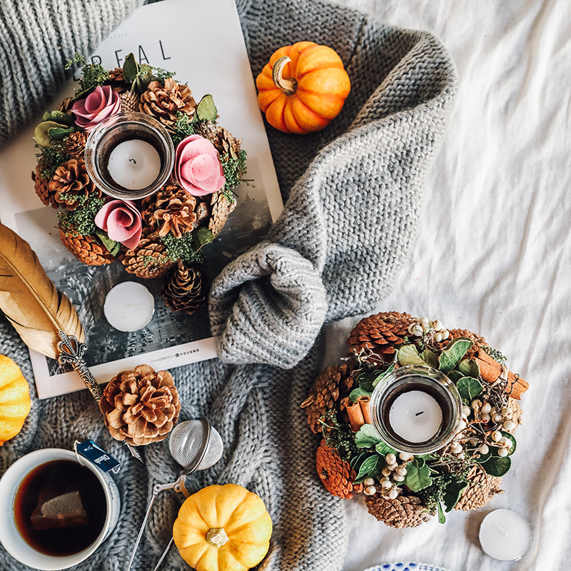 Autumn-themed decor with wreaths, candles, pumpkins, and a book on a textured surface.