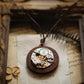 Steampunk-style pocket watch necklace on an old book page with dried leaves.