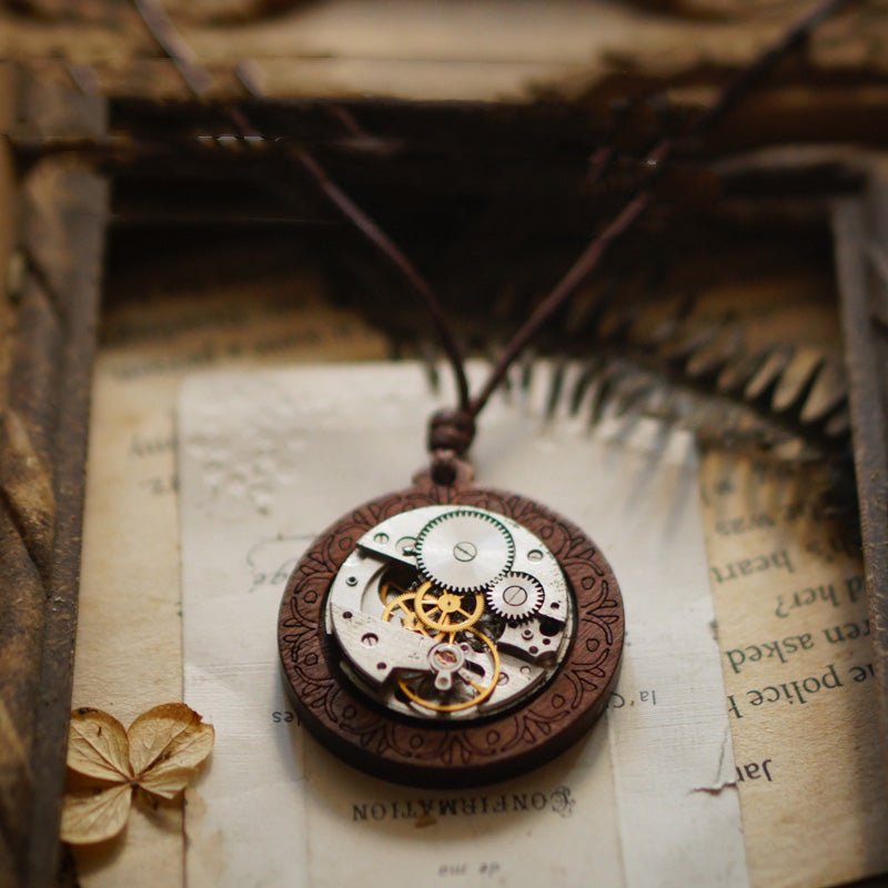 Steampunk-style pocket watch necklace on an old book page with dried leaves.