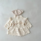Knitted baby dress with lace details and matching hat on a light gray background
