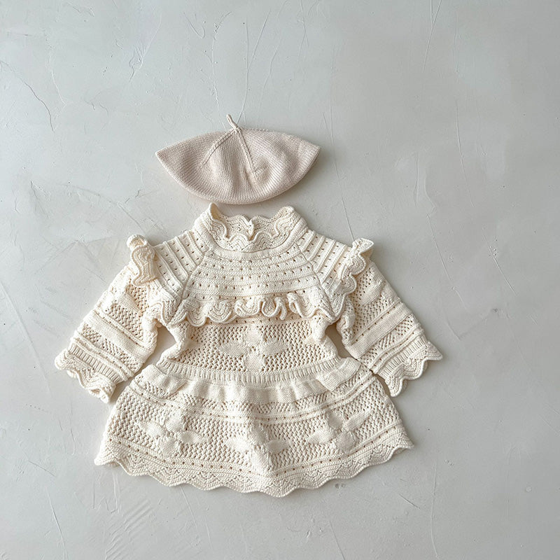Knitted baby dress with lace details and matching hat on a light gray background