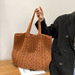 Person holding a brown textured tote bag on a wooden surface with a neutral background